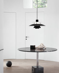 Black pendant light above a round dining table in a minimalist interior with a clean modern aesthetic.