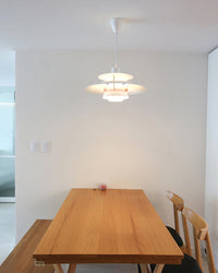 Modern white pendant light with layered shades installed above a wooden dining table, creating a clean focal point in a minimalist dining room.