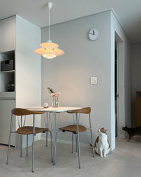 Warm white layered pendant light hanging above a small round dining table in a minimalist dining area.