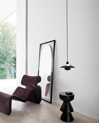 Black pendant light hanging in a minimalist living space with a lounge chair and modern decor.
